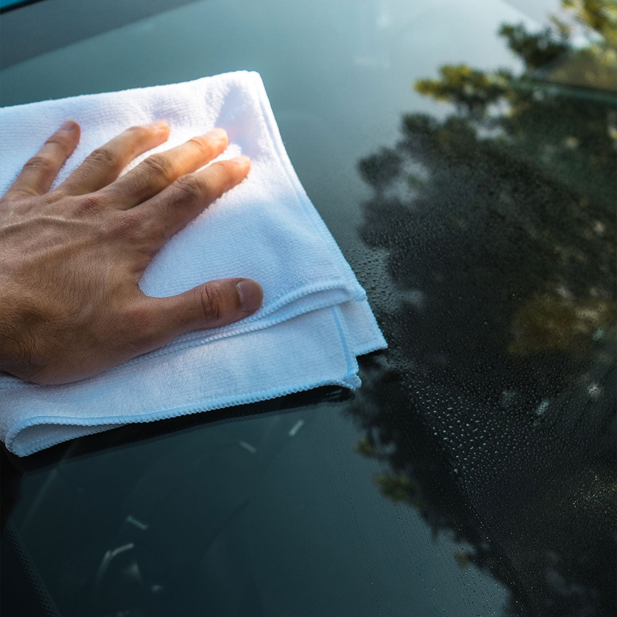 glass cleaner being wiped away with white microfibre and hand on front wind screen