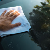 glass cleaner being wiped away with white microfibre and hand on front wind screen