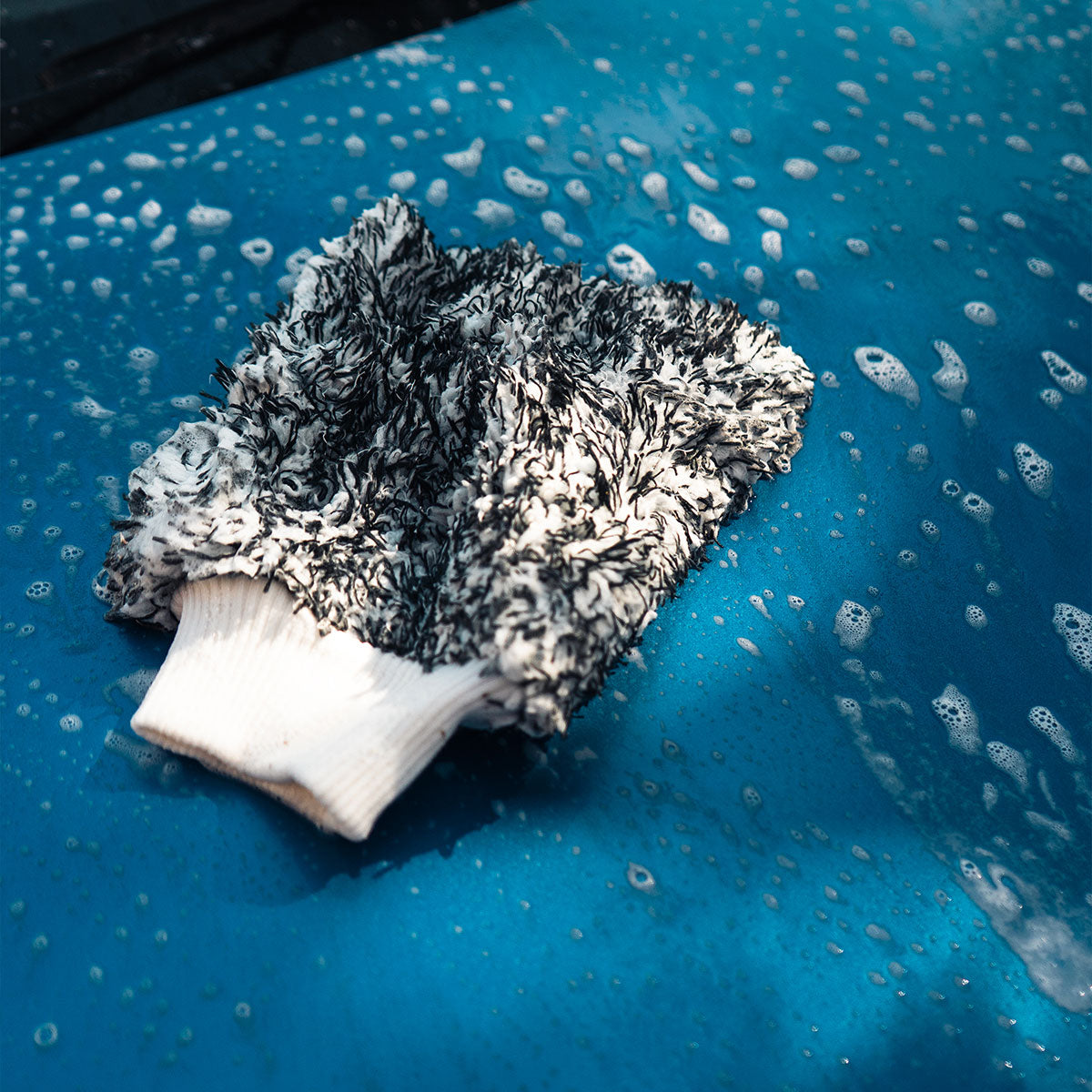 product shot of microfibre wash mitt with suds covering blue car being cleaned